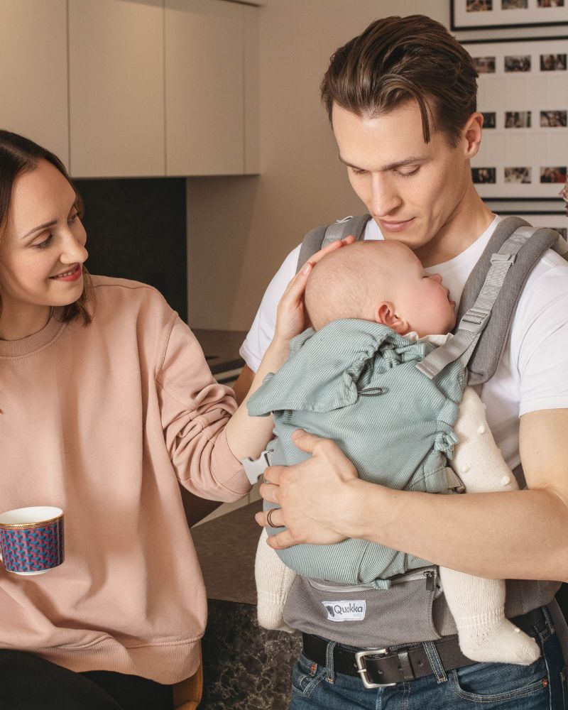 papas porteando en casa a su beb&eacute; dormido en posici&oacute;n ergon&oacute;mica en una mochila Quokkababy